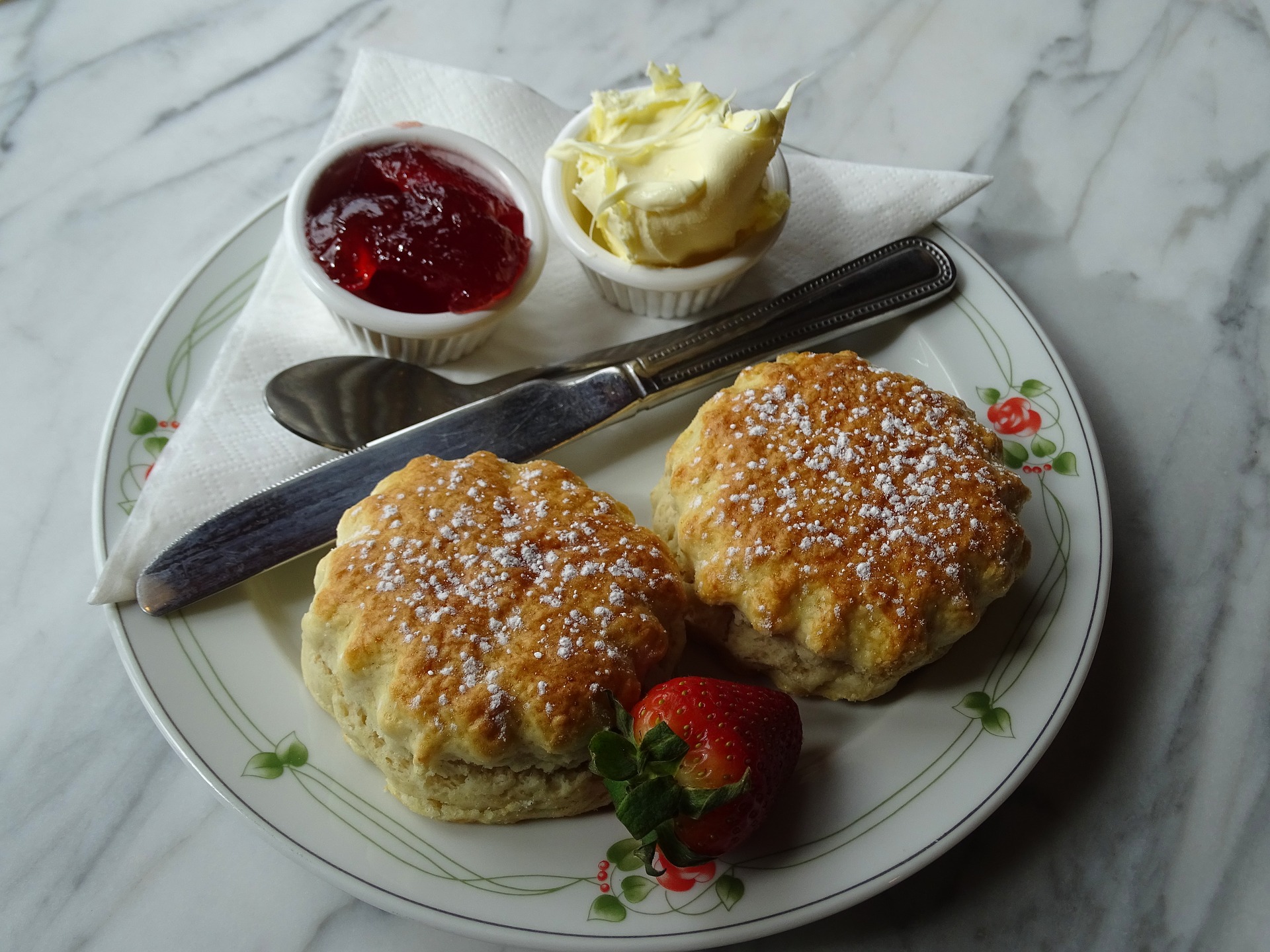 Two scones, served on a pretty plate with a mini bowl each of jam and clotted cream