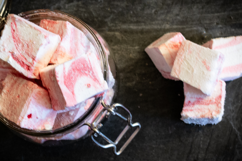 Pink and white swirled marshmallows in a jar, with a pile to the right