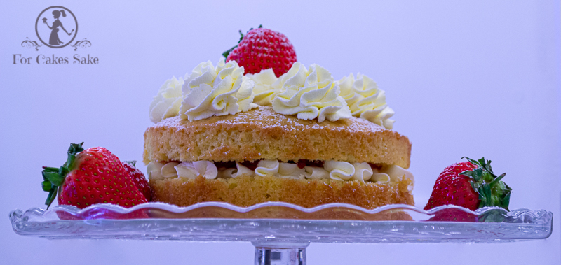 A Vcitoria Sandwich cake on a cake stand with cream and strawberries.